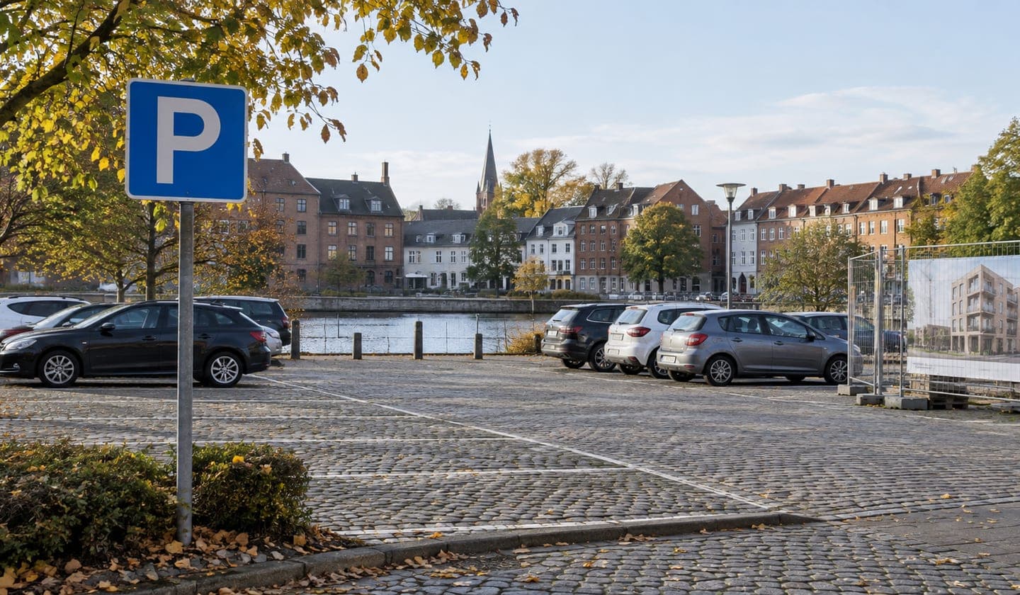 Kommunal parkeringsplads i en dansk bymidte med blåt p-skilt og biler langs vandet.