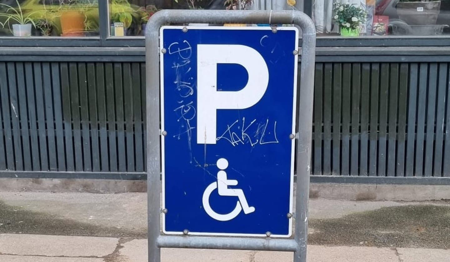 Et blåt handicapparkeringsskilt foran en bygning i København.