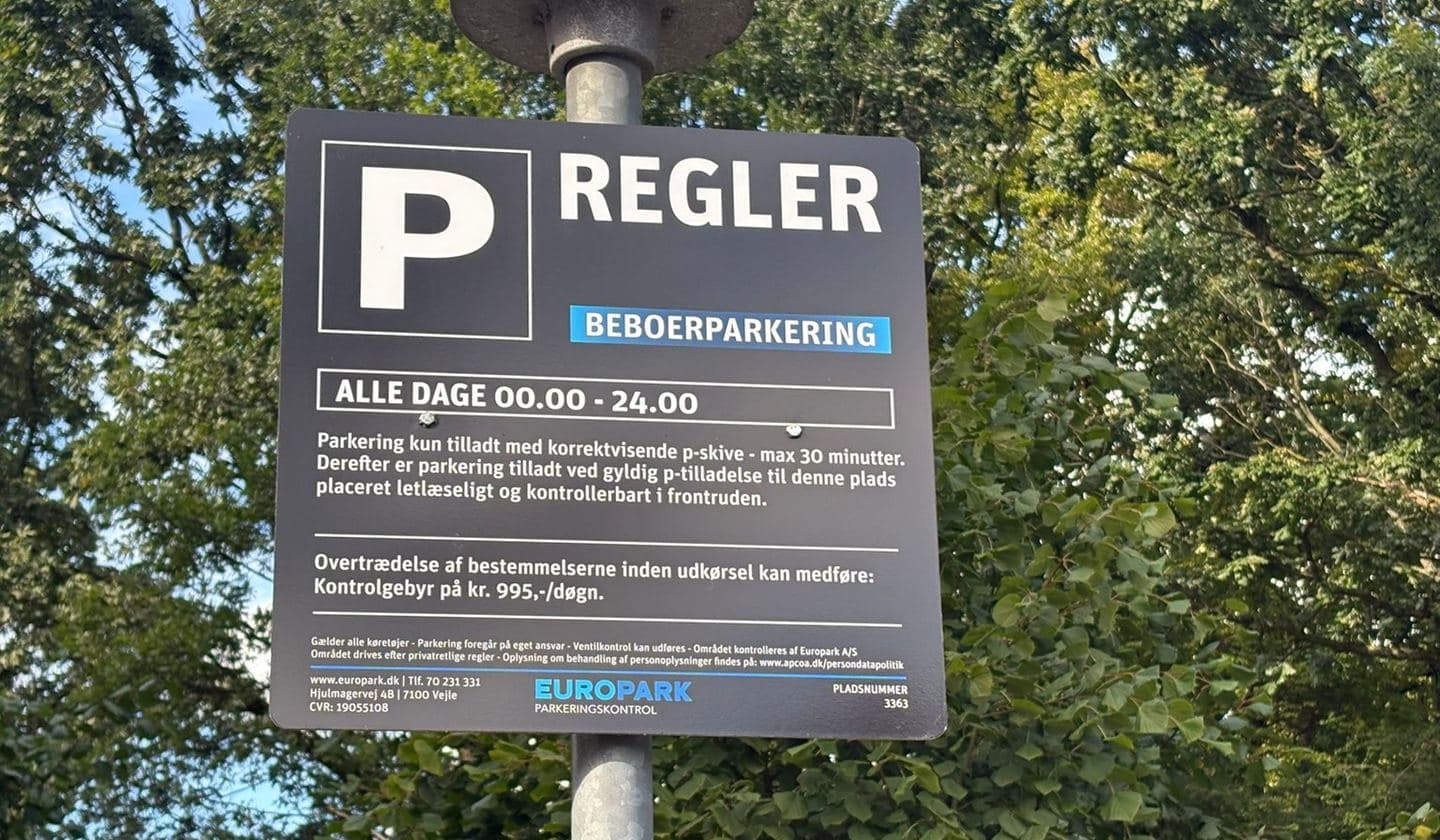 Parkeringsskilt ved en dansk vej med biler i baggrunden.